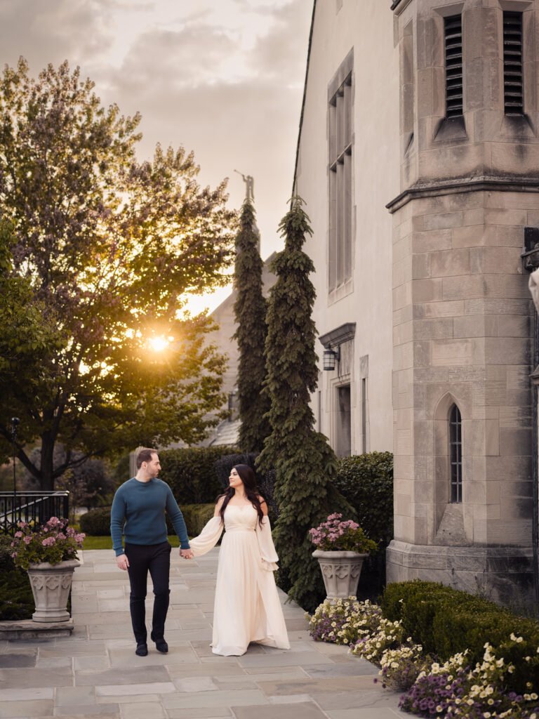 Couple holding hands while walking through a garden pathway at sunset during an elegant engagement session.