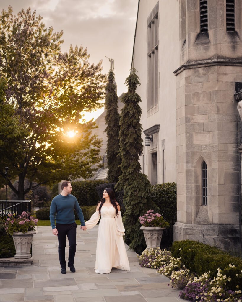 Couple holding hands while walking through a garden pathway at sunset during an elegant engagement session.